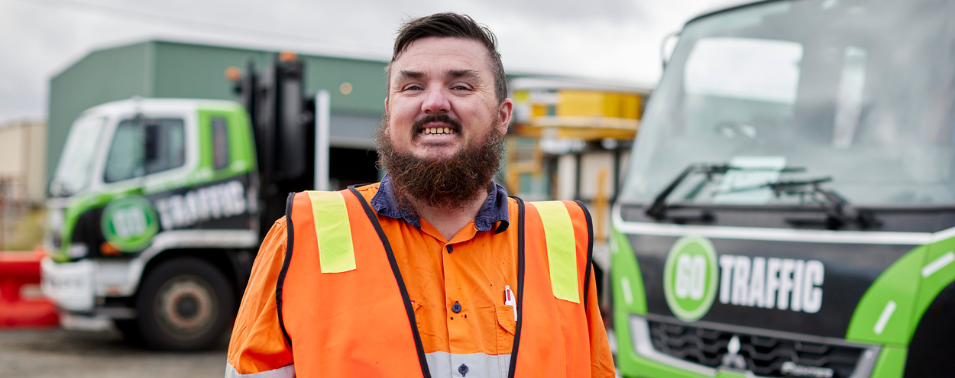 James in high visibility workwear, smiling in front of Go Traffic trucks