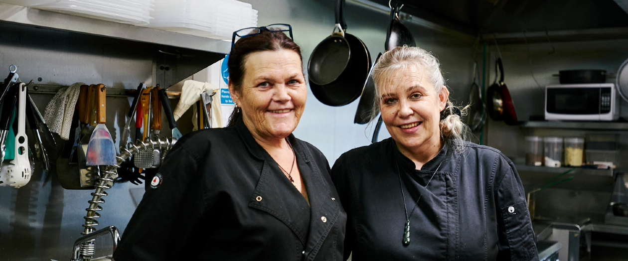 Two cooks smiling at the camera in a commercial kitchen